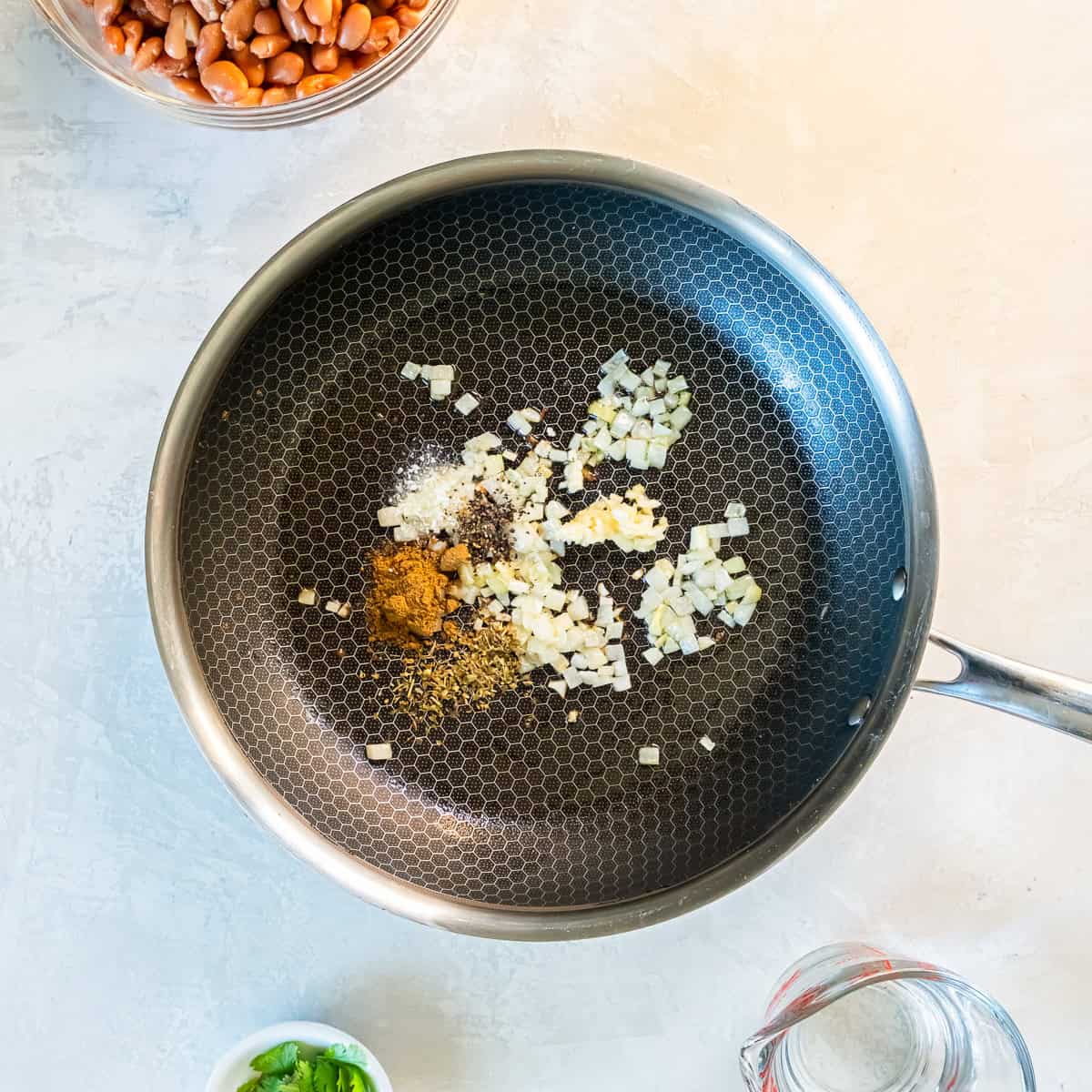 Aromatics and spices added to a skillet including onion, garlic, cumin, oregano, salt, and pepper