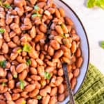 Easy seasoned pinto beans garnished with fresh cilantro in a shallow bowl with a serving spoon.