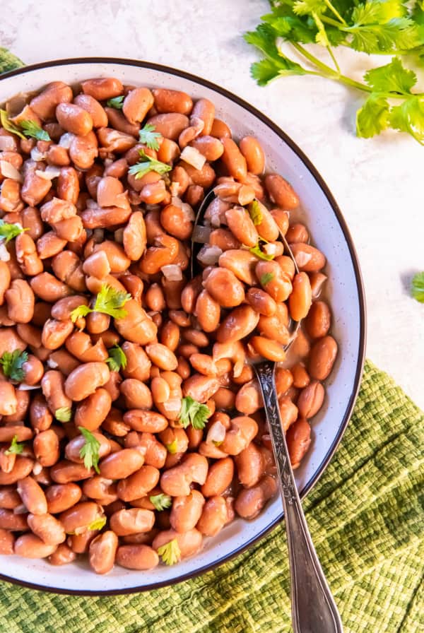 Easy seasoned pinto beans garnished with fresh cilantro in a shallow bowl with a serving spoon.