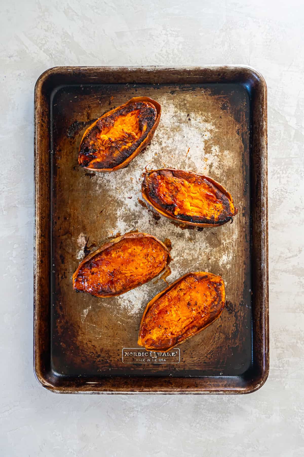 Sweet potato halves on a baking sheet, cut side up and seasoned with salt and black pepper.
