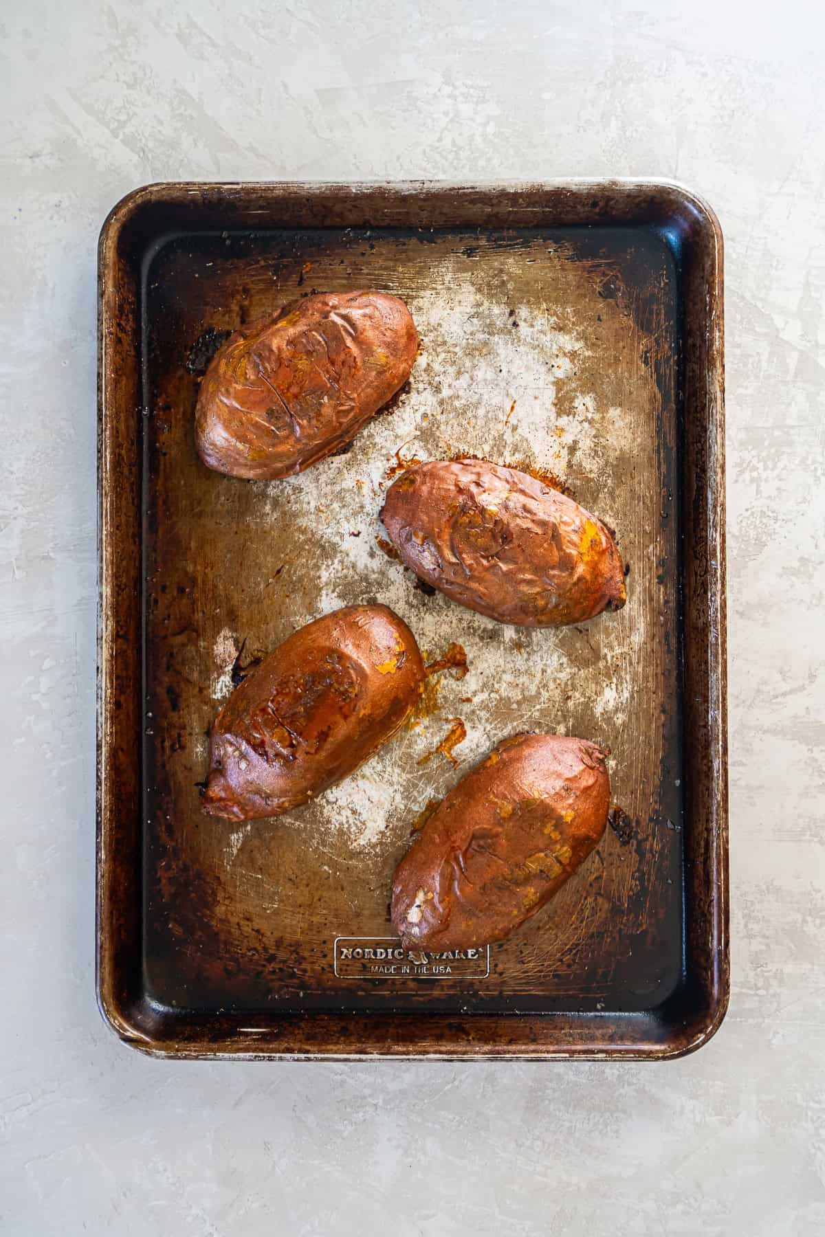 Whole sweet potatoes coated with olive oil on a baking sheet before roasting,