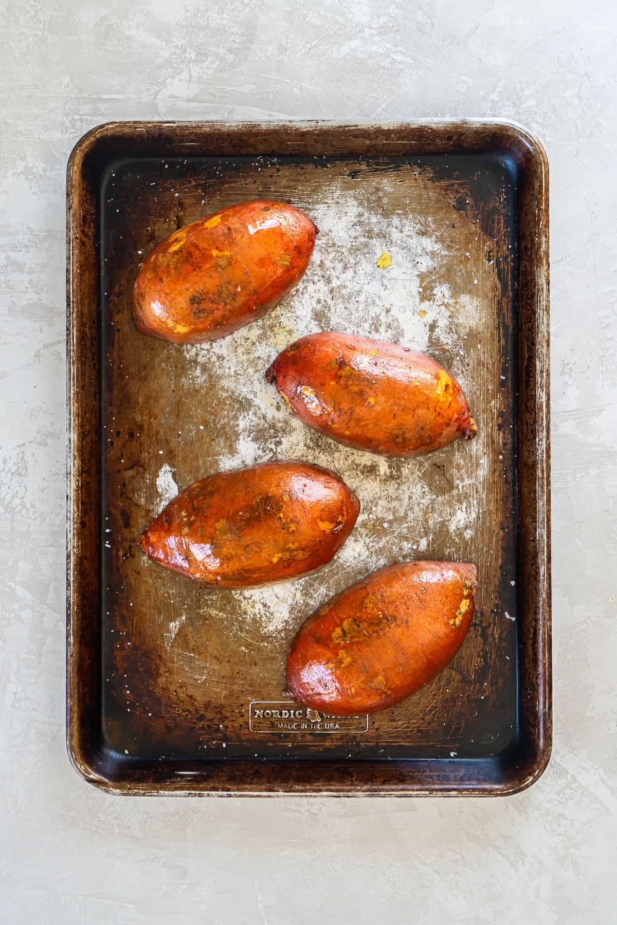 Roasted whole sweet potato halves on a baking sheet with softened skins after baking.