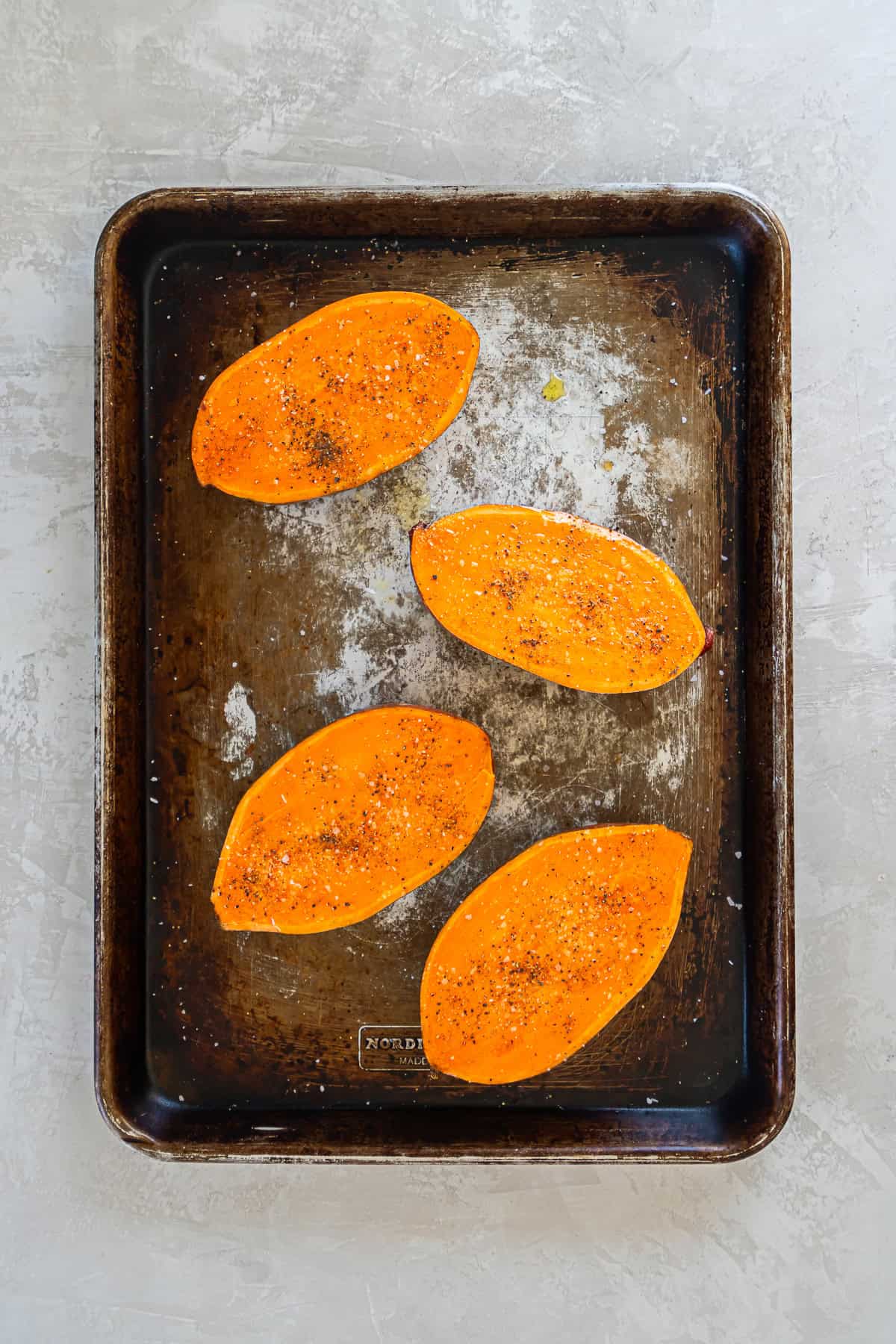 Baked sweet potato halves cut side up showing deeply caramelized surfaces on a baking sheet.
