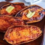 Roasted sweet potato halves with caramelized edges and a pat of melting butter, served on a wooden platter.