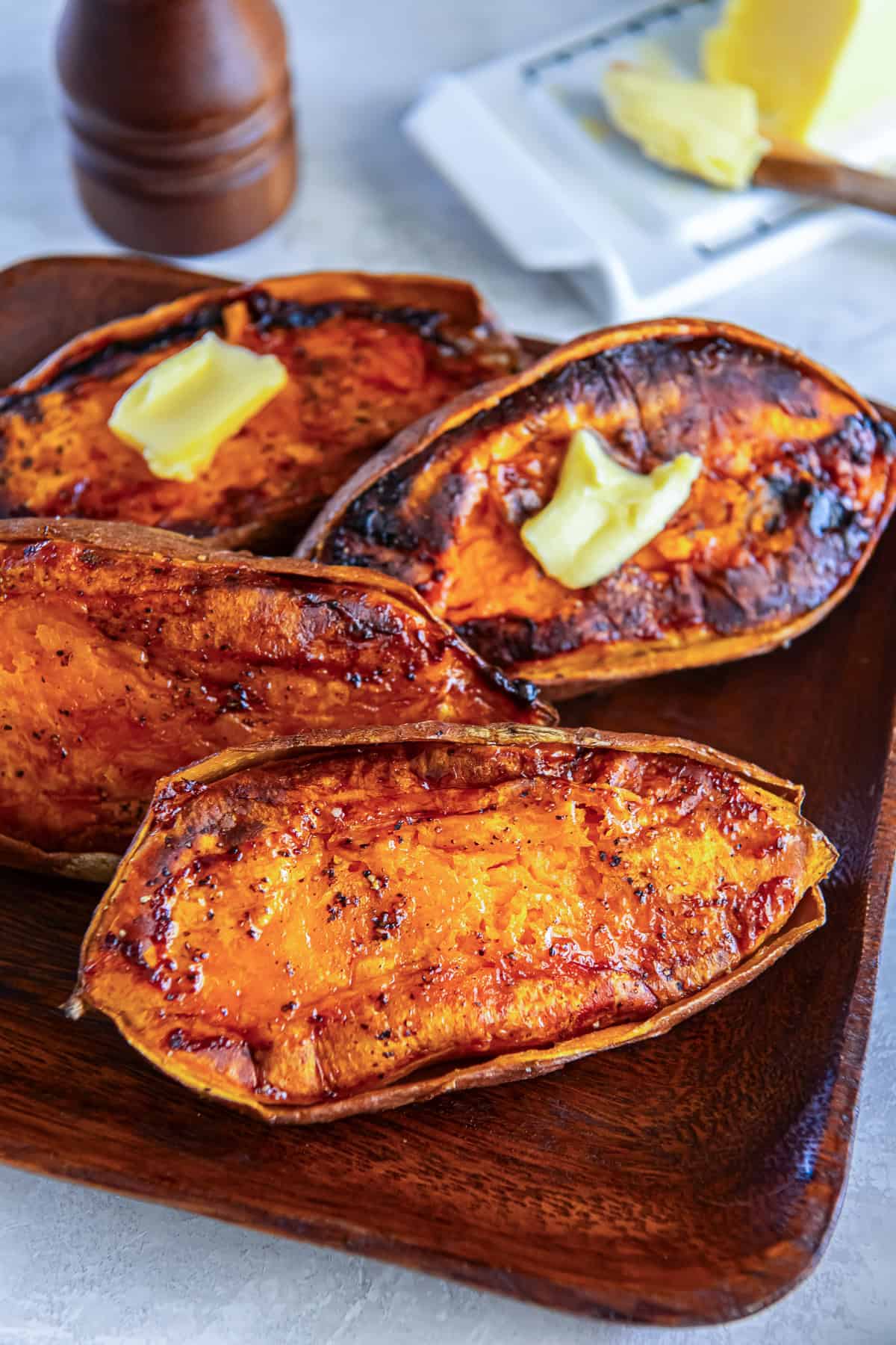 Roasted sweet potato halves with caramelized edges and a pat of melting butter, served on a wooden platter.