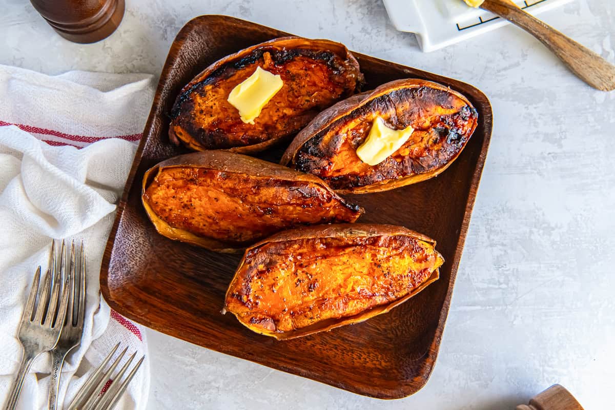 caramelized baked sweet potato halves on a wooden platter, topped with melting butter,