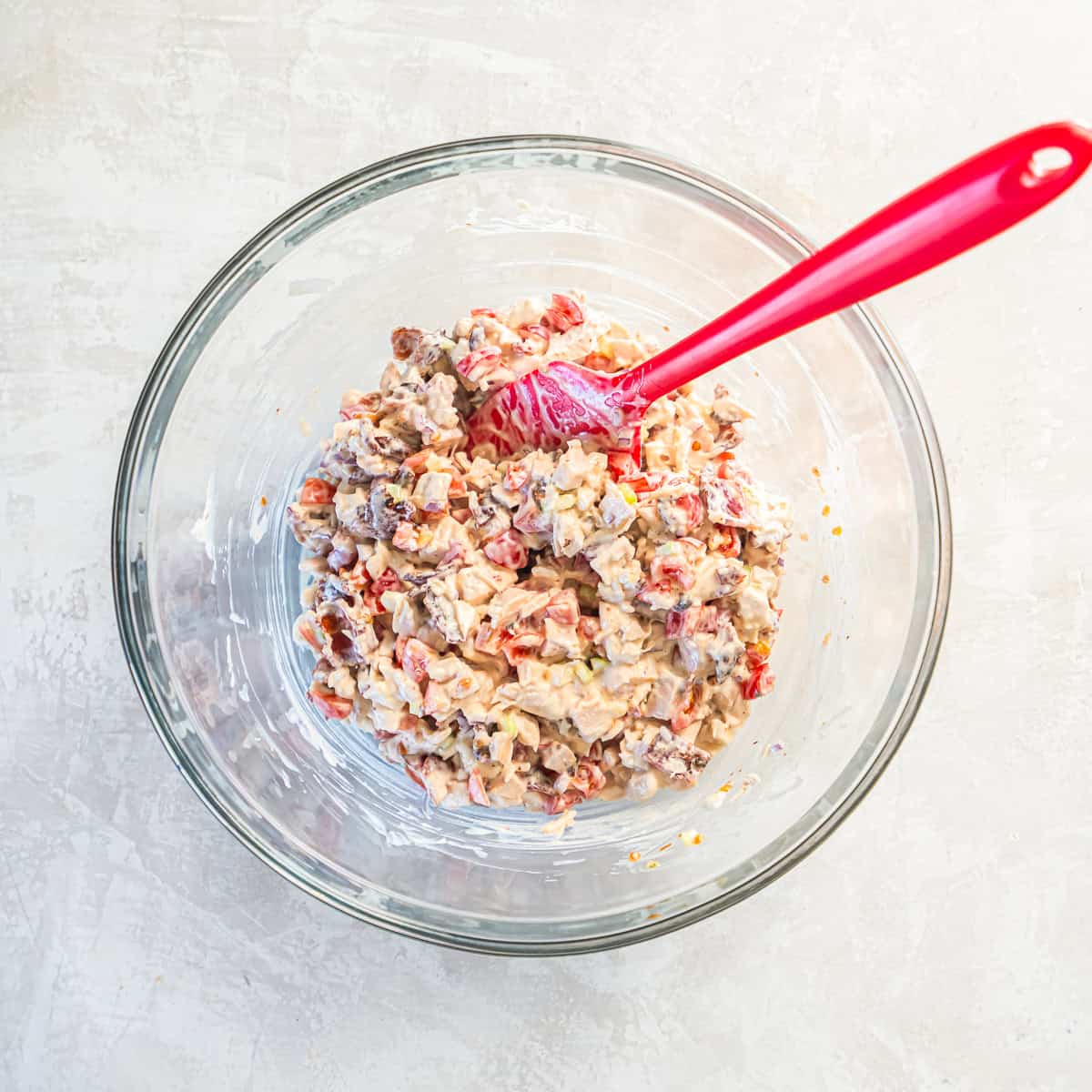 BLT chicken salad fully mixed in a glass bowl with a red spatula.