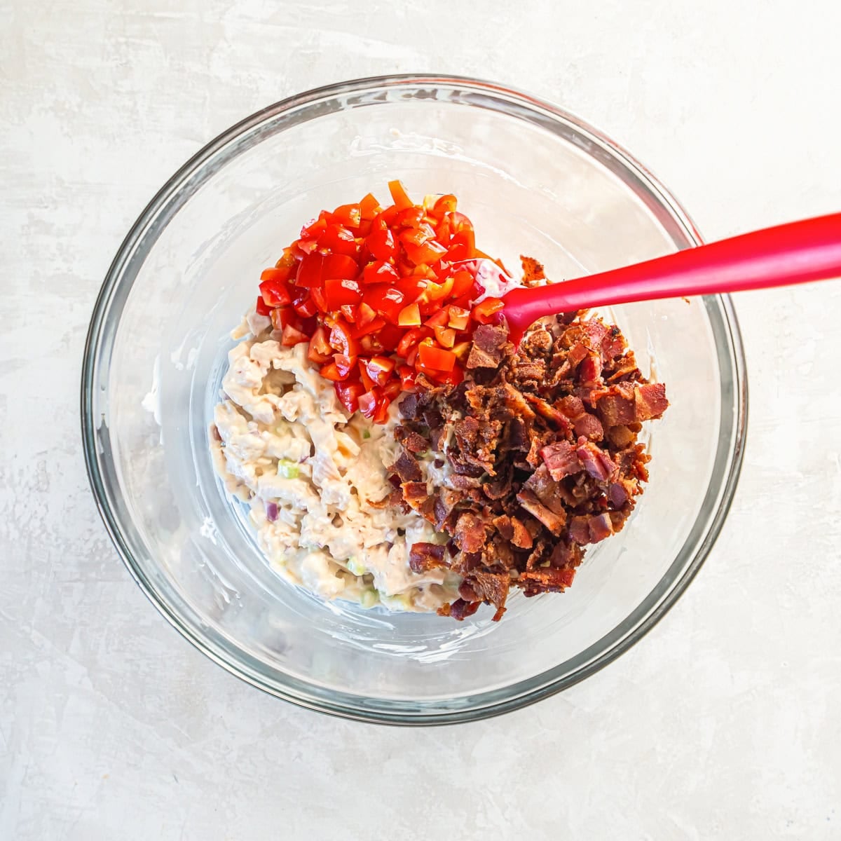 Chopped bacon and diced tomatoes added to chicken salad mixture in a bowl.