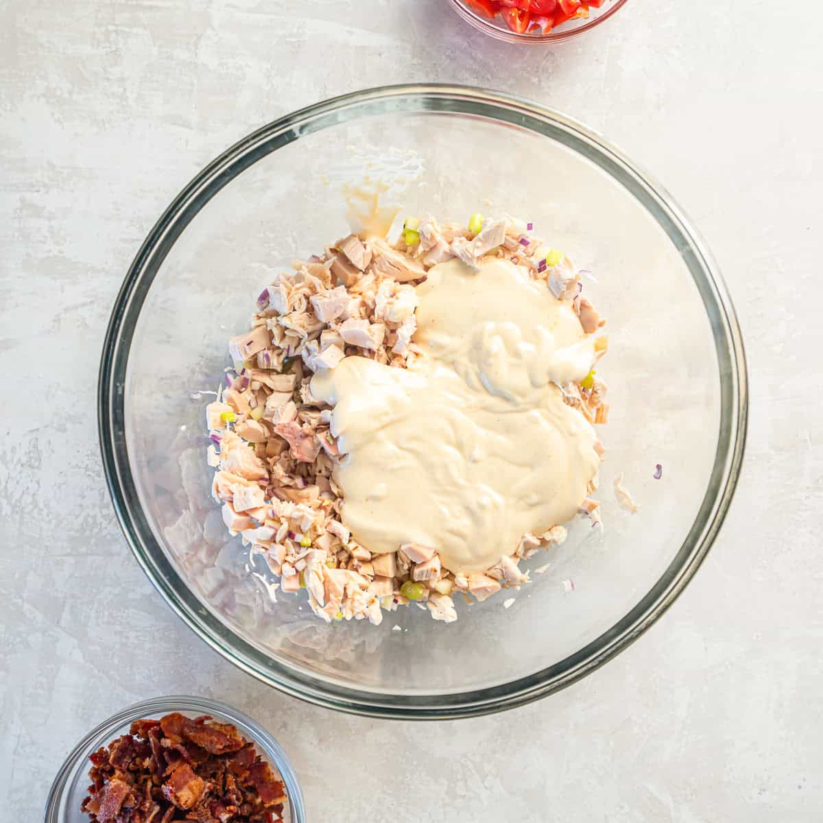 Dressing poured over chopped chicken mixture in a glass bowl.
