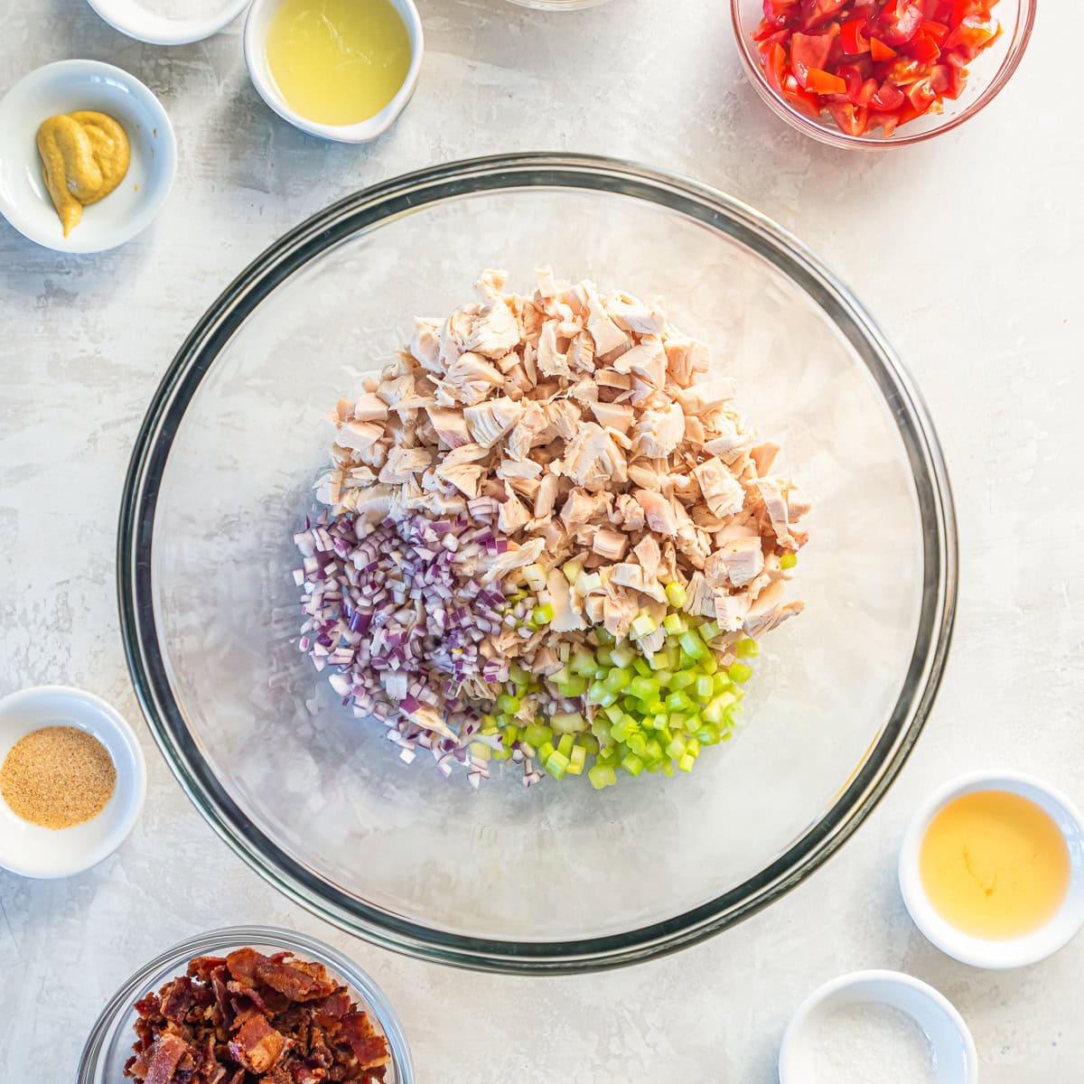 Chopped rotisserie chicken, celery, and red onion combined in a large glass mixing bowl.