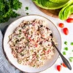 BLT chicken salad in a bowl with a spoon, garnished with fresh parsley and black pepper, served with romaine lettuce leaves for wraps.