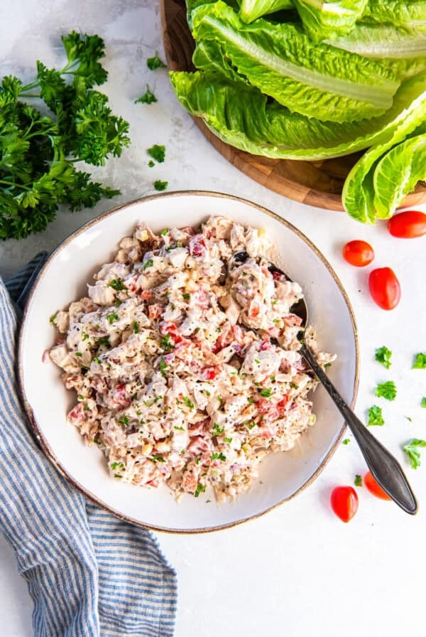 BLT chicken salad in a bowl with a spoon, garnished with fresh parsley and black pepper, served with romaine lettuce leaves for wraps.