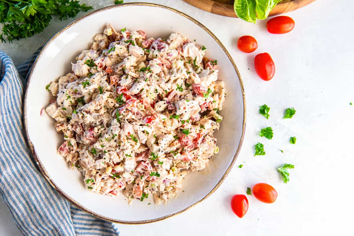 BLT chicken salad in a bowl garnished with fresh parsley and black pepper, with grape tomatoes and romaine lettuce leaves on the side.