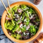 Butter lettuce salad with snap peas, radishes, goat cheese, and chives in a wooden salad bowl with salad spoons on a light countertop.
