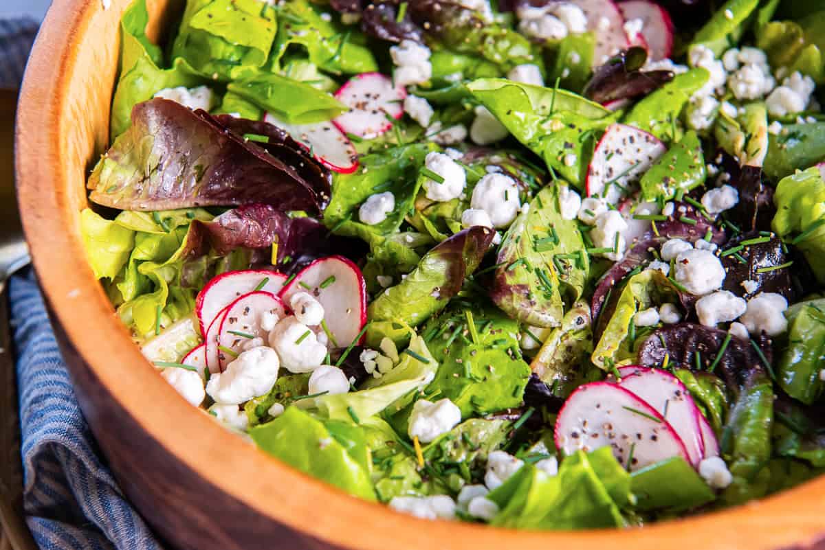 Butter lettuce salad with snap peas, radishes and goat cheese in a wood salad bowl