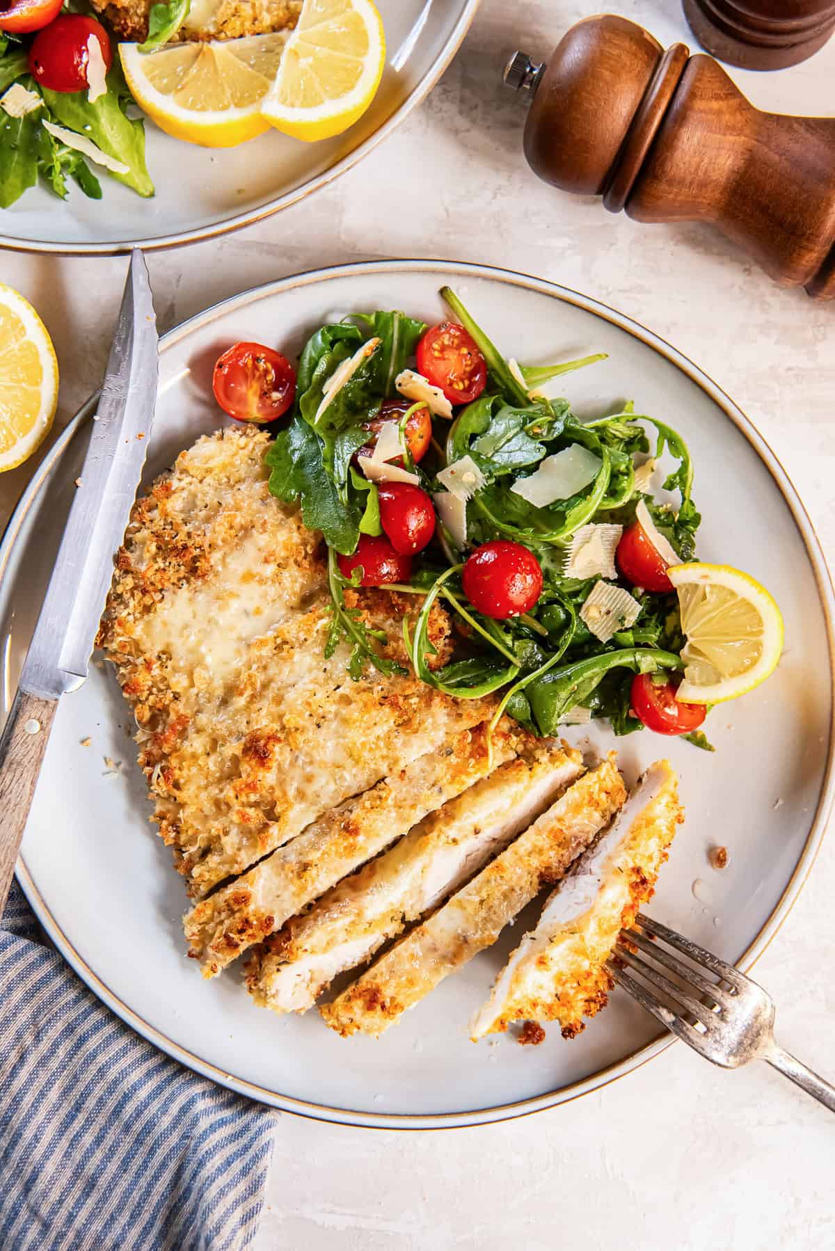 Breaded Chicken Milanese with melted Parmesan served with arugula salad, cherry tomatoes, and lemon wedges.