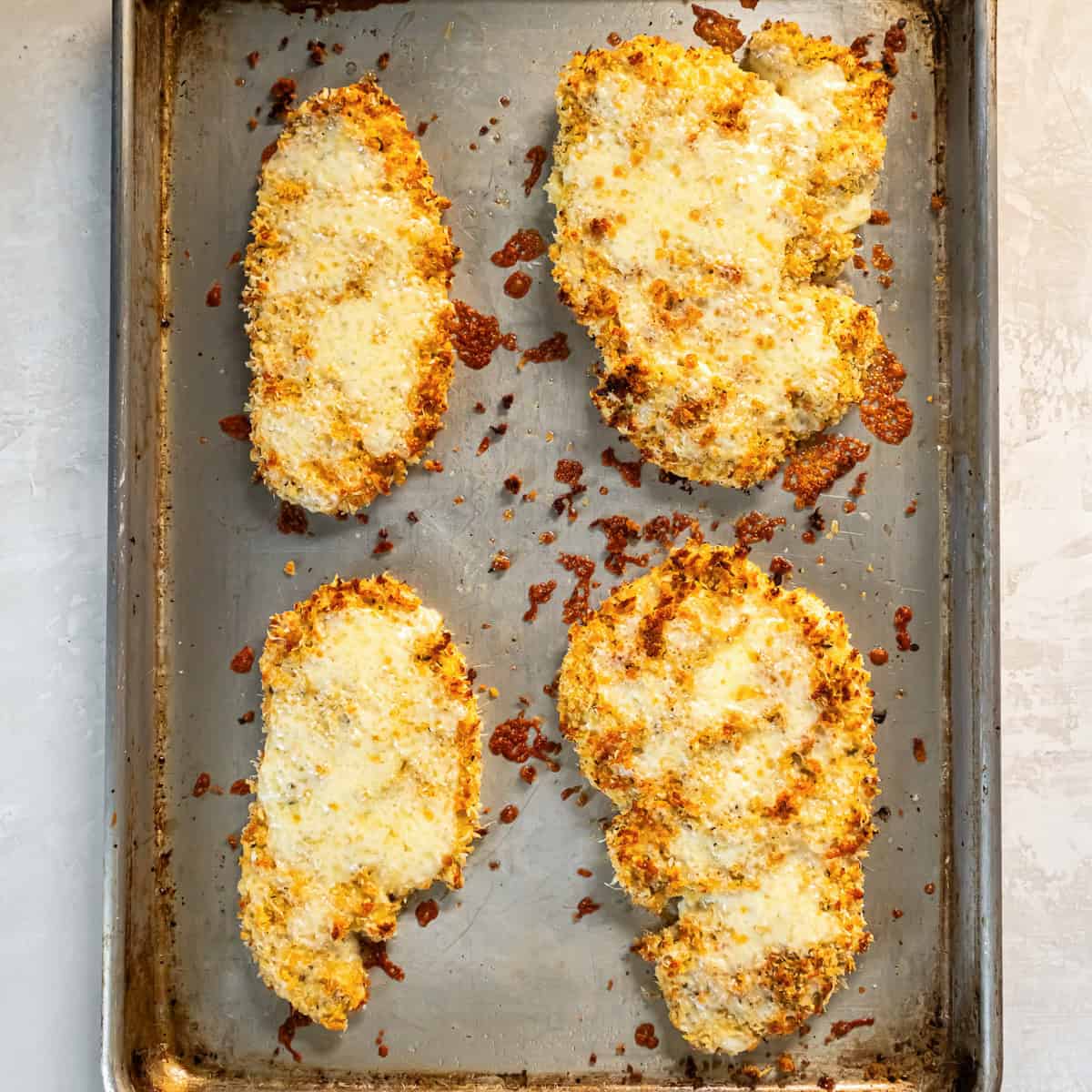 Breaded chicken cutlets topped with melted cheese on a baking sheet after baking.