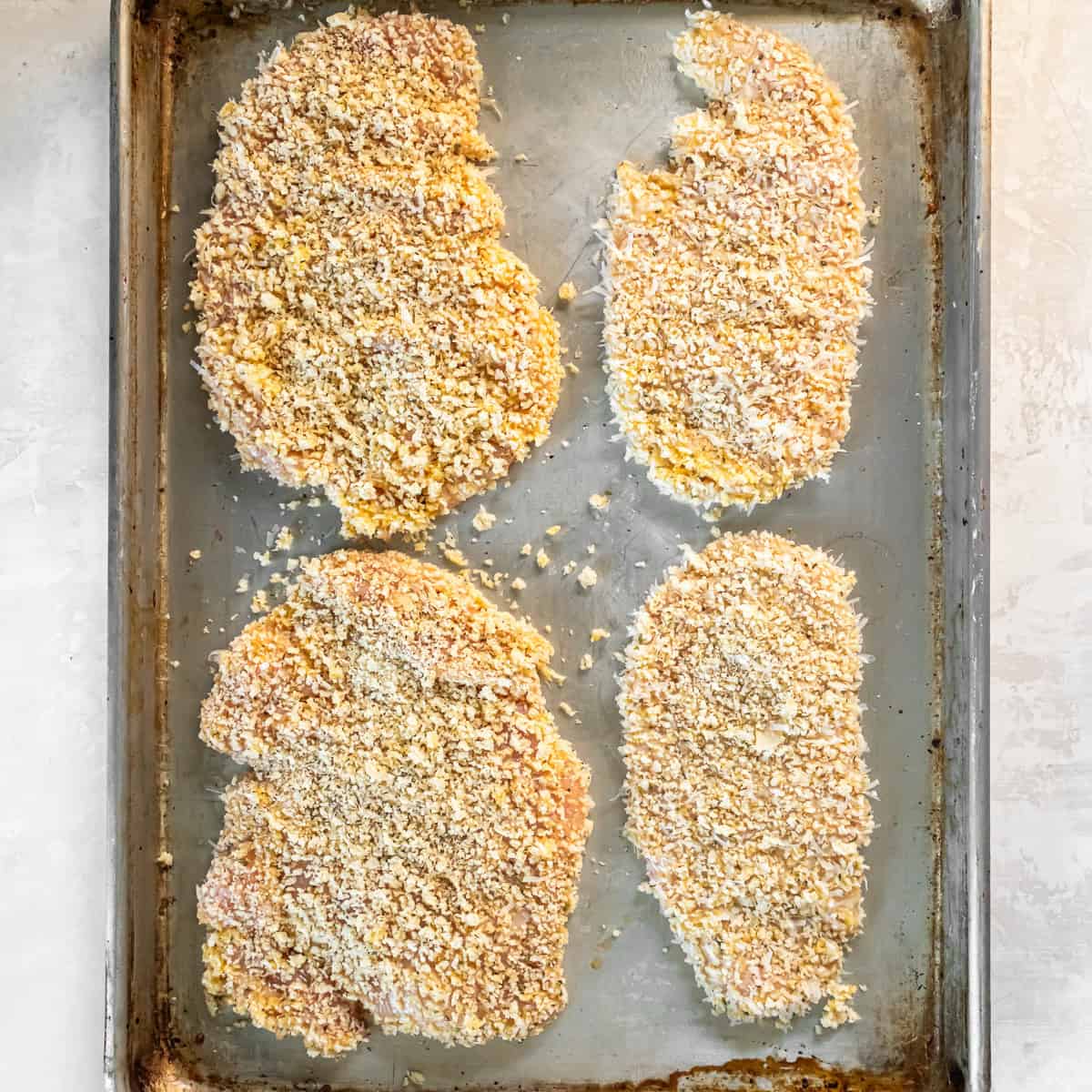 Breaded chicken cutlets arranged on a baking sheet before baking.
