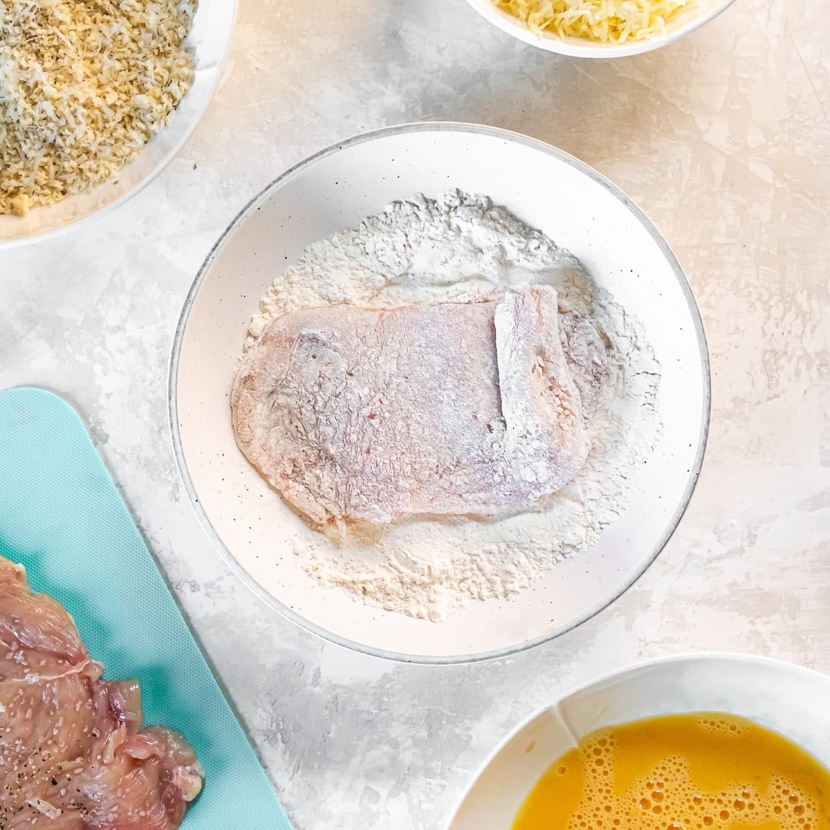 Chicken cutlet dredged in flour as the first step in breading for Chicken Milanese.