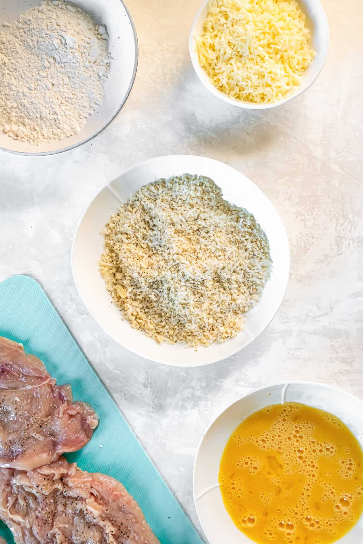 Chicken Milanese breading station with flour, beaten eggs, and panko mixed with Parmesan for coating the chicken.