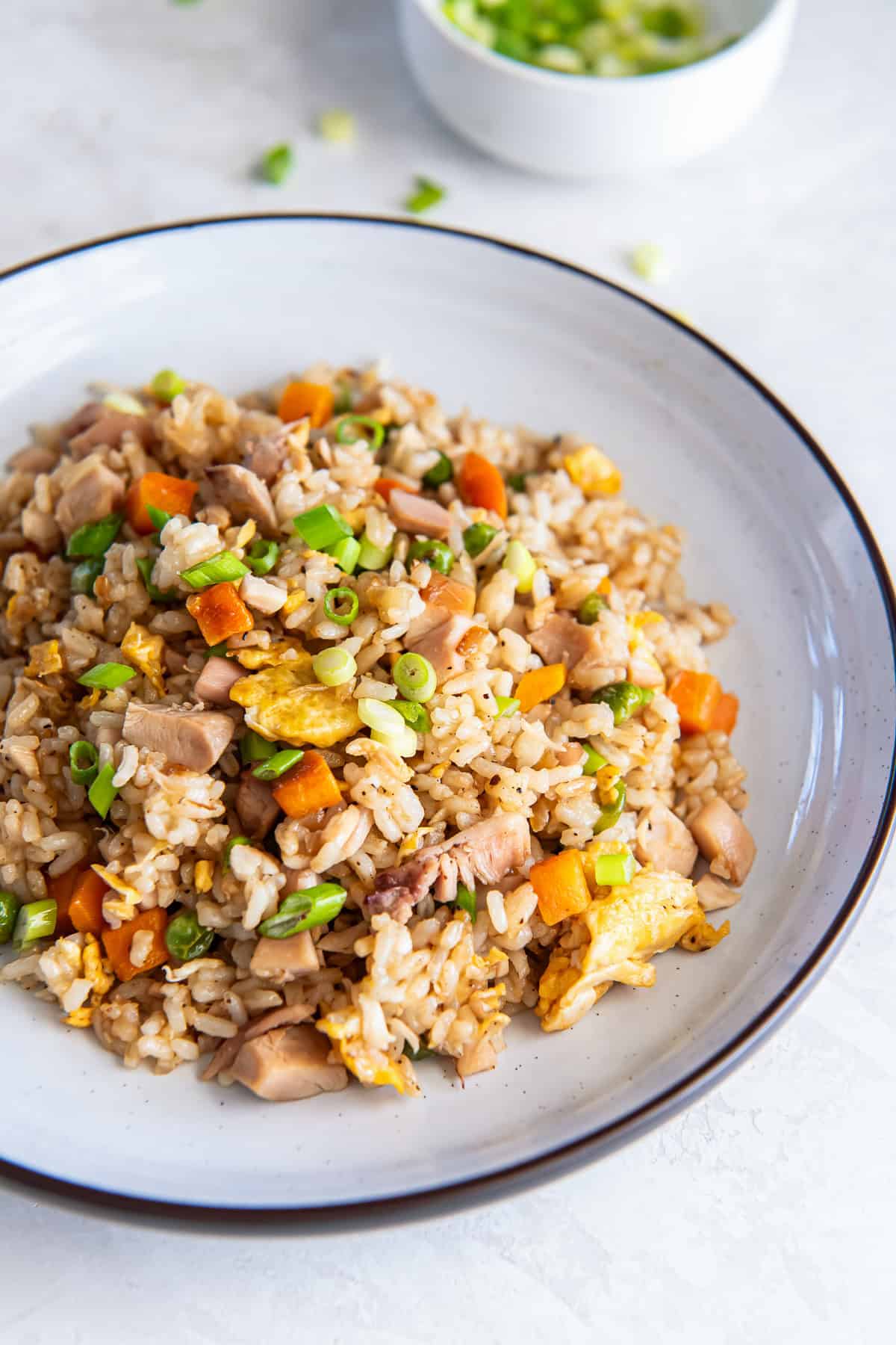 Chicken fried rice with rotisserie chicken, peas, carrots, scrambled eggs, and green onions served on a white plate.