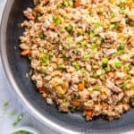 Chicken fried rice in a skillet with vegetables, scrambled eggs, chopped chicken, and green onions.