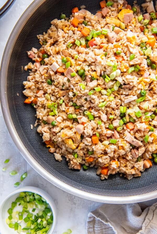 Chicken fried rice in a skillet with vegetables, scrambled eggs, chopped chicken, and green onions.