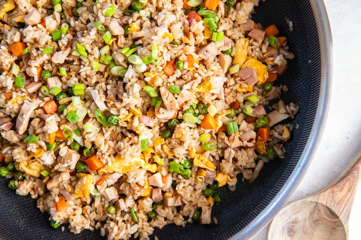 Chicken fried rice with peas, carrots, scrambled eggs, rotisserie chicken, and green onions in a skillet.