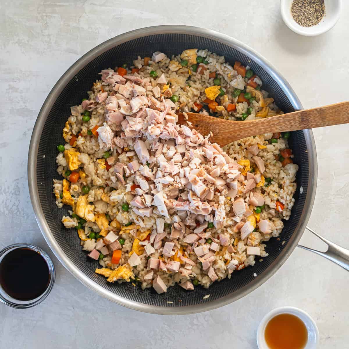 Chopped rotisserie chicken added to fried rice with eggs and vegetables in a skillet.