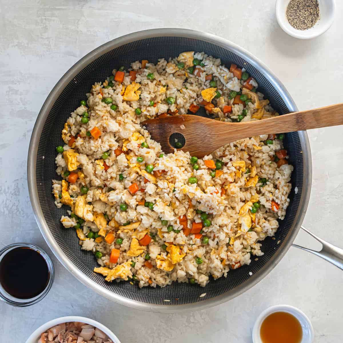 Cooked jasmine rice and scrambled eggs mixed with peas and carrots in a skillet.