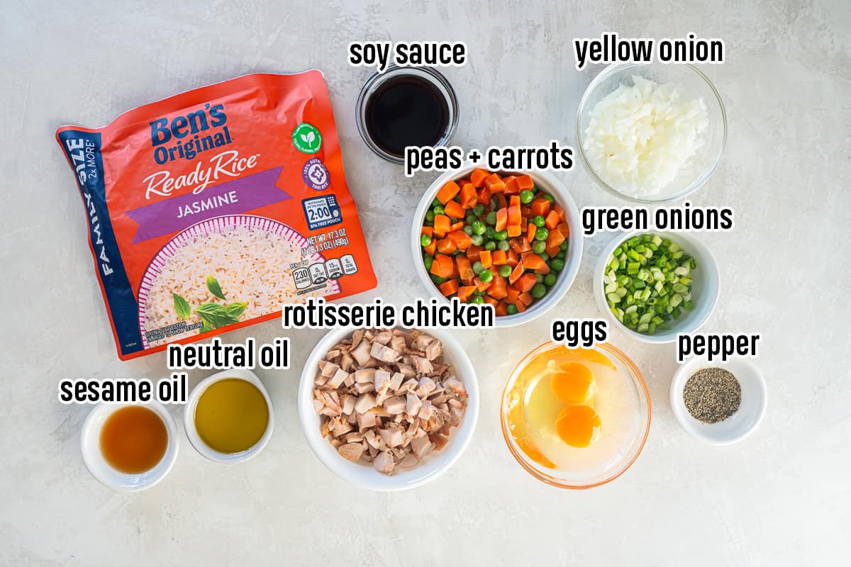 Ingredients for Easy Chicken Fried Rice arranged on a countertop including Ben&rsquo;s Original ready rice, rotisserie chicken, eggs, peas and carrots, yellow onion, green onions, soy sauce, sesame oil, neutral oil, and black pepper.