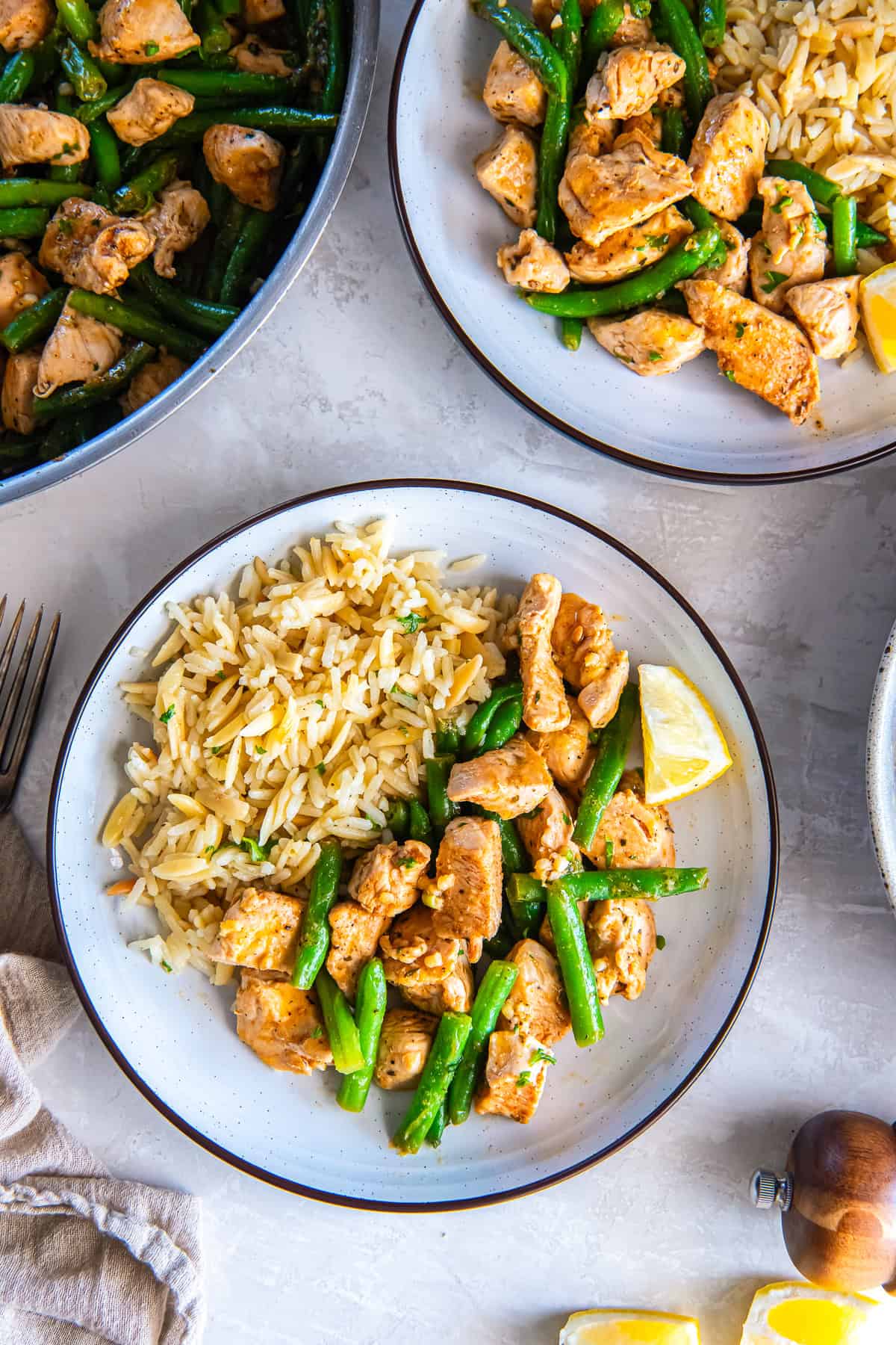Garlic butter chicken and green beans served with rice on a plate with a lemon wedge, with a skillet of chicken and green beans in the background.