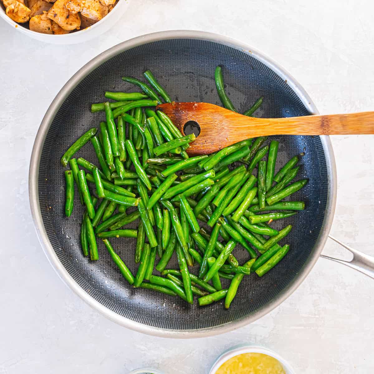 Green beans cooking in a skillet with a small amount of liquid to steam until tender-crisp.