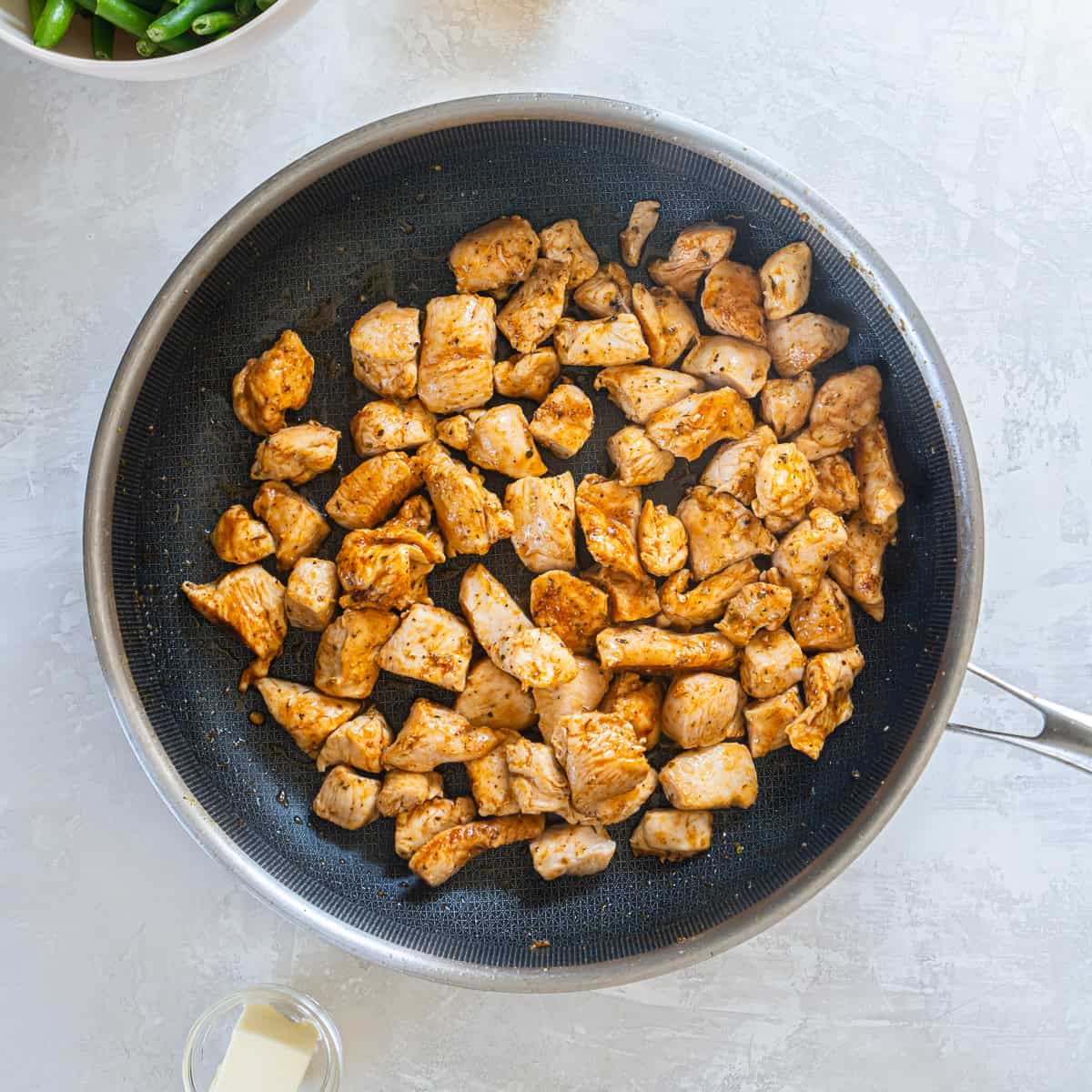 Seasoned chicken pieces cooking in a skillet until browned.