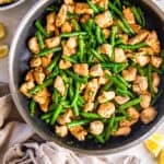 Garlic butter chicken with green beans in a skillet with rice and lemon wedges on the side.