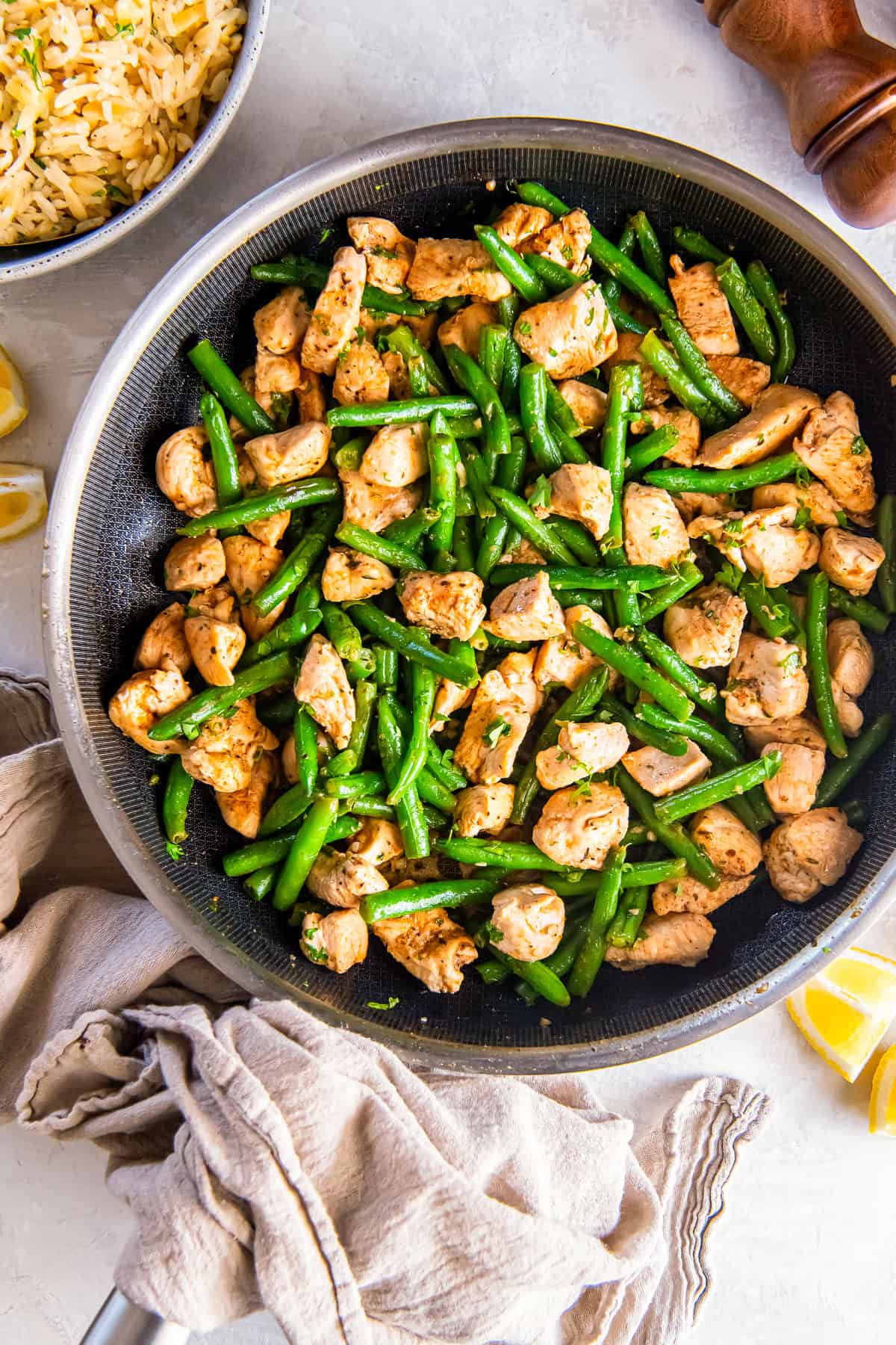 Garlic butter chicken with green beans in a skillet with rice and lemon wedges on the side.
