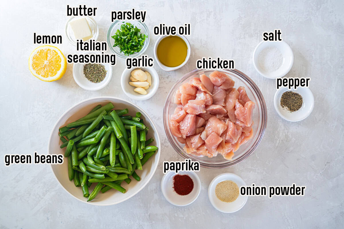 Ingredients for garlic butter chicken with green beans arranged on a light surface including chicken, green beans, garlic, butter, lemon, olive oil, herbs, and spices.