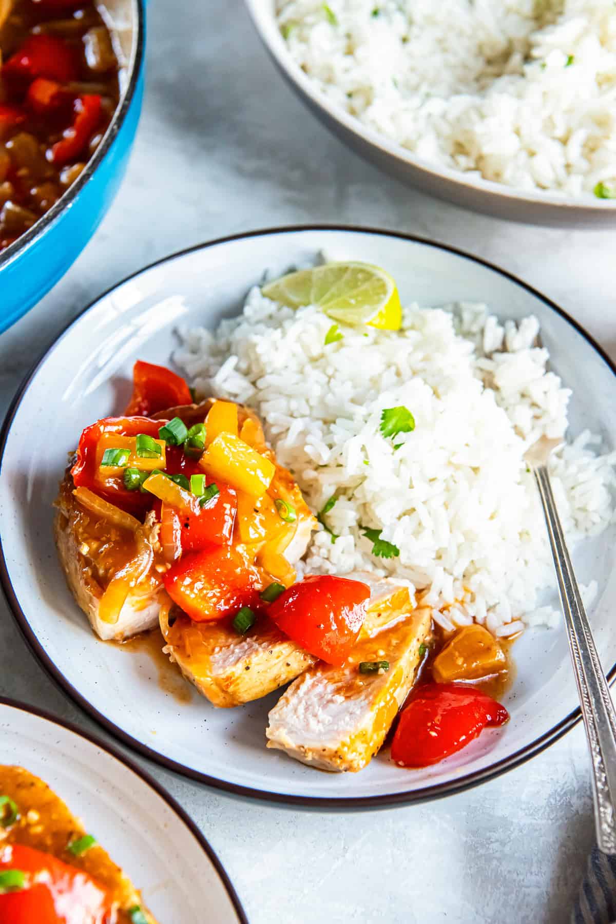 Sliced Hawaiian pork chop topped with pineapple tidbits, red bell pepper, and onion in a glossy sauce, served with white rice and a lime wedge.
