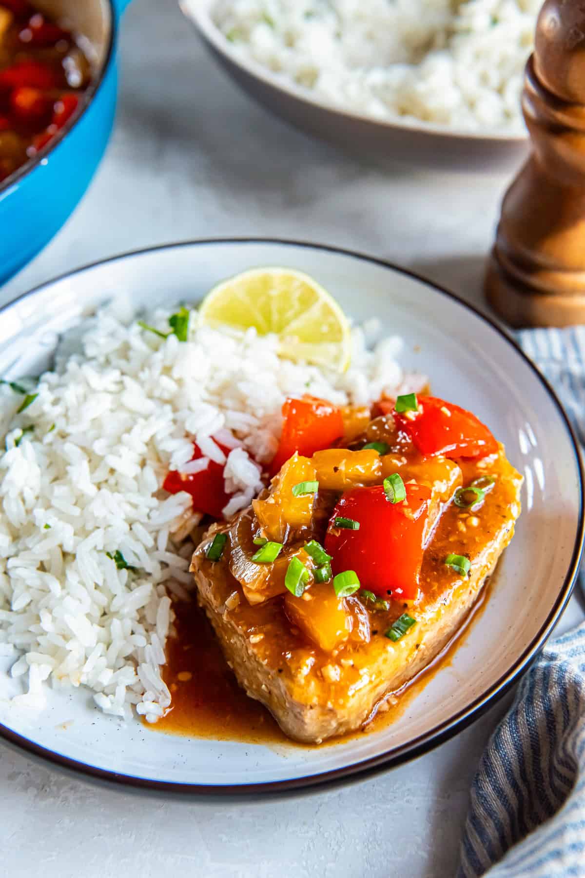 Hawaiian pork chops in pineapple sauce with red bell pepper and onion, served with white rice, with the skillet and additional plates on the table.