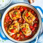 Skillet of Hawaiian pork chops in a glossy pineapple sauce with red bell pepper, onion, and pineapple tidbits, served with a bowl of white rice and lime wedges on the side.