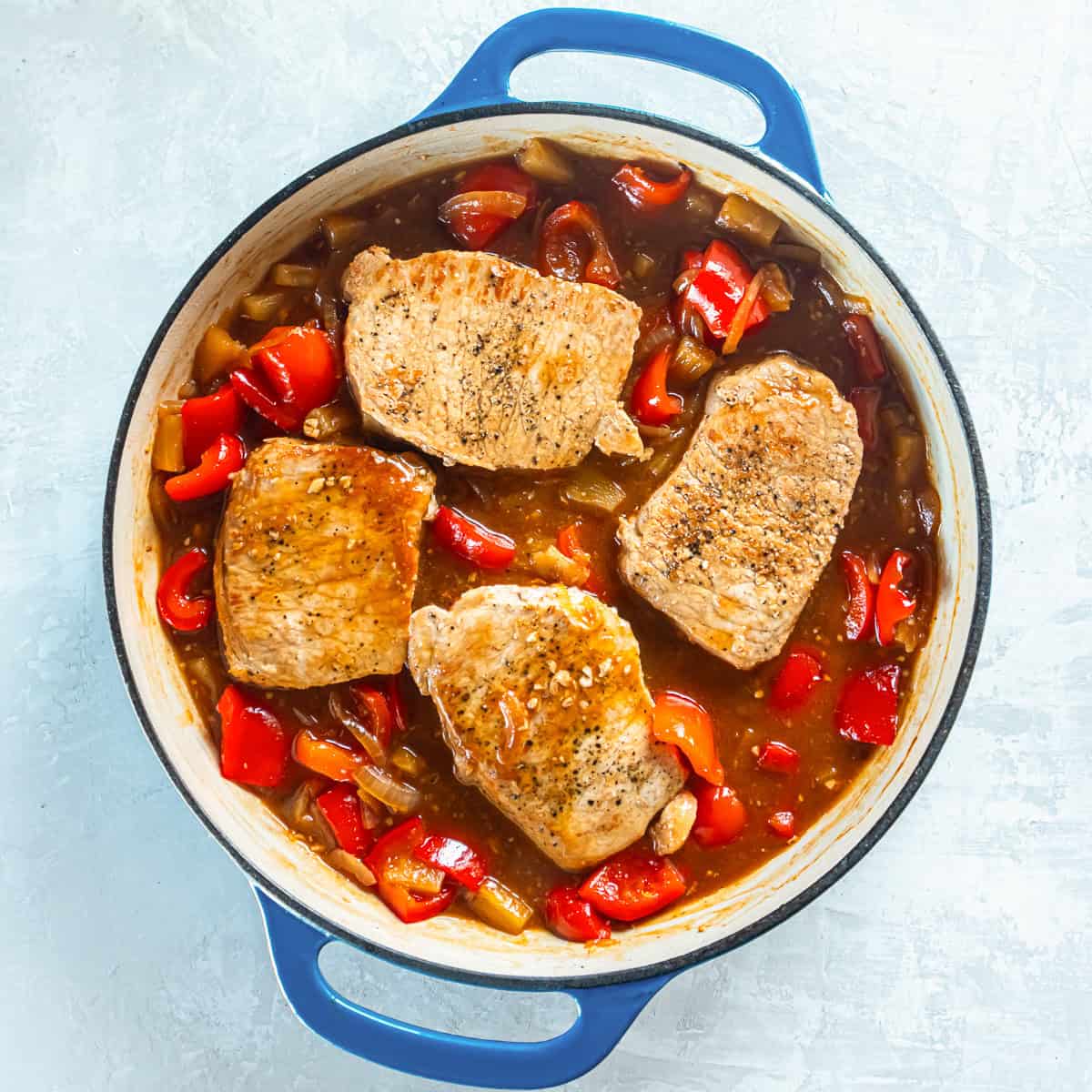 Cooked pork chops on top of a Hawaiian sauce, red bell peppers, onions, and pineapple in a skillet.