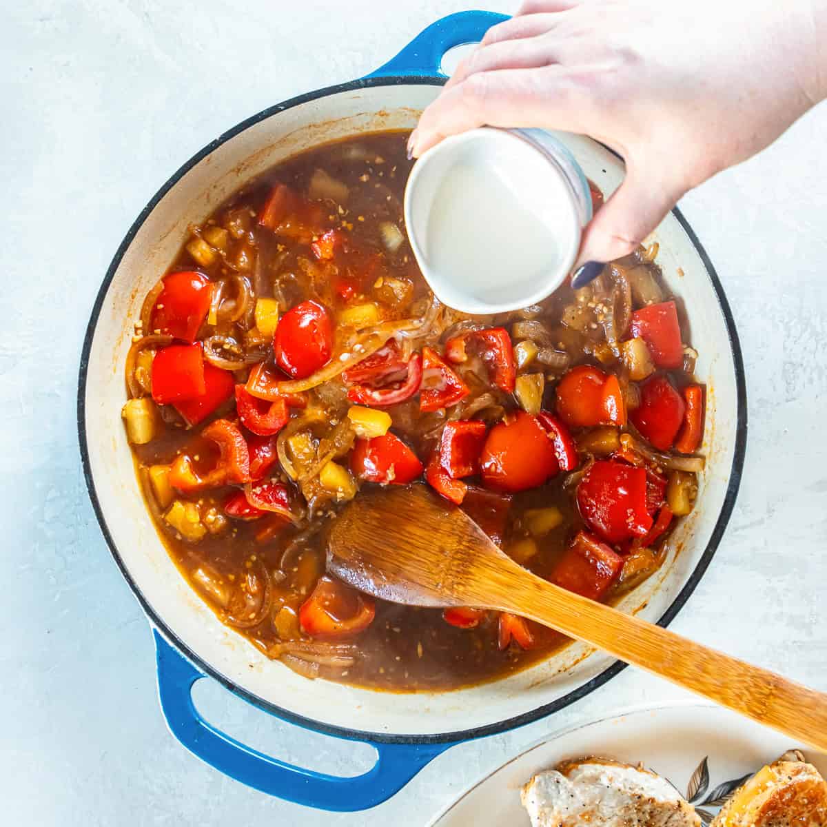 A cornstarch slurry being poured into a skillet with a sauce made with bell pepper, onion, and pineapple.