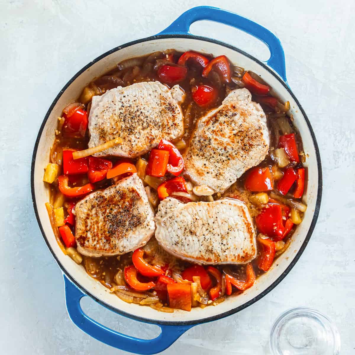 Browned pork chops on top of a mixture of cooked red bell pepper, onion, and pineapple.