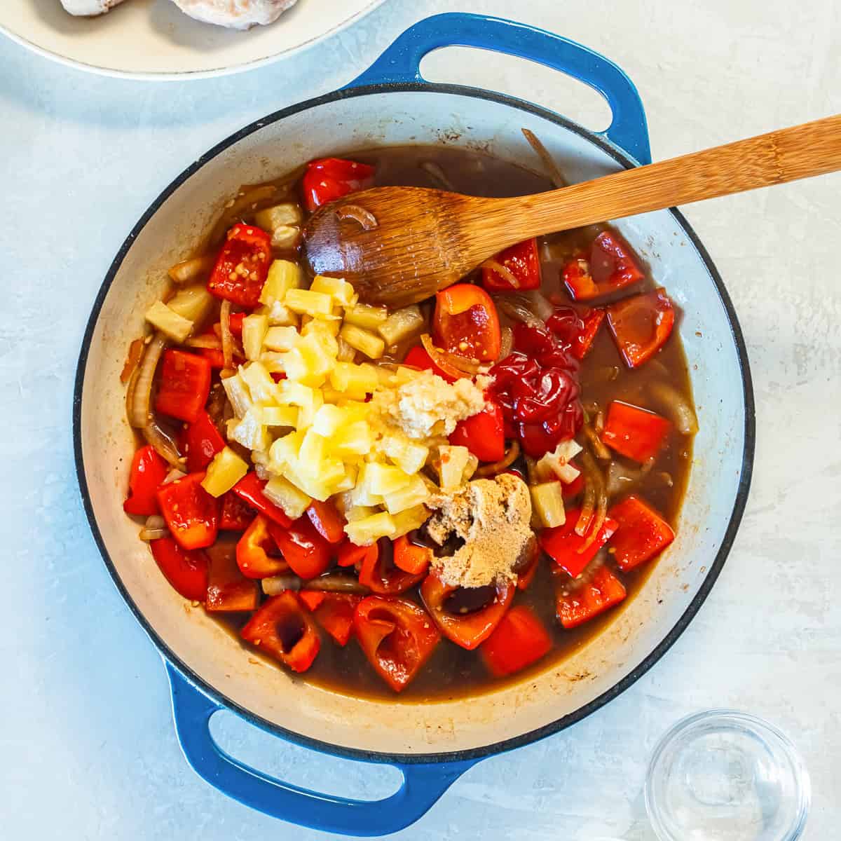 Cooked red bell peppers and onions in a skillet topped with pineapple tidbits.
