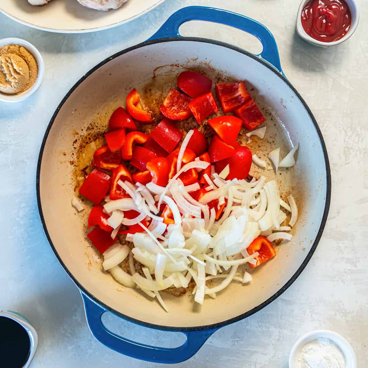 Red bell peppers and sliced onion in a skillet.