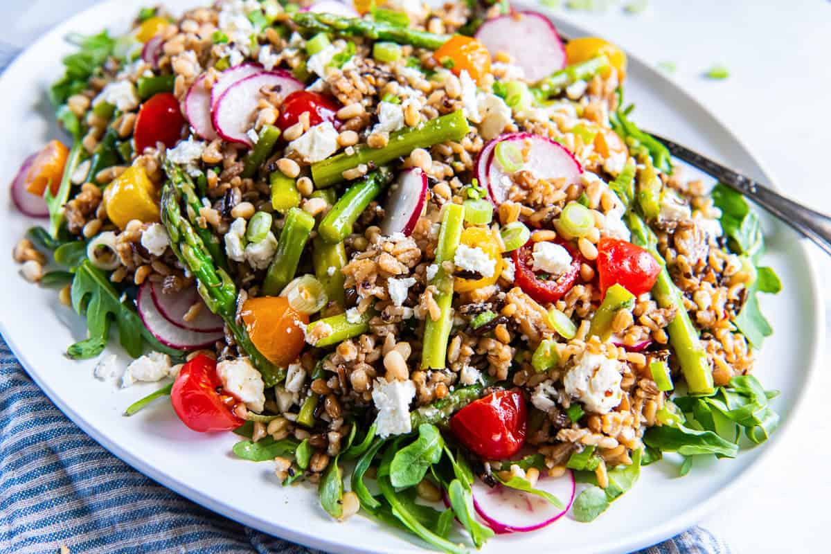 Spring grain salad with asparagus, radishes, cherry tomatoes, goat cheese, and pine nuts served over arugula on a platter.