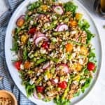 Spring grain salad with asparagus, radishes, cherry tomatoes, goat cheese, pine nuts, and arugula tossed in apple cider vinaigrette on a serving platter.