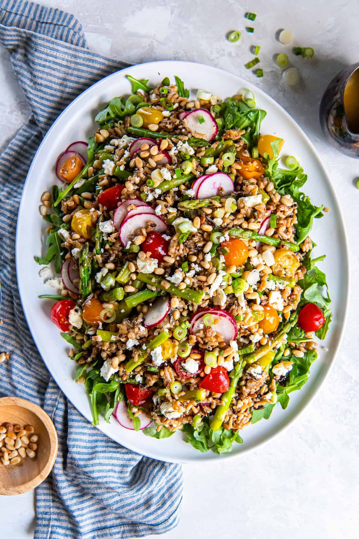 Spring grain salad with asparagus, radishes, cherry tomatoes, goat cheese, pine nuts, and arugula tossed in apple cider vinaigrette on a serving platter.