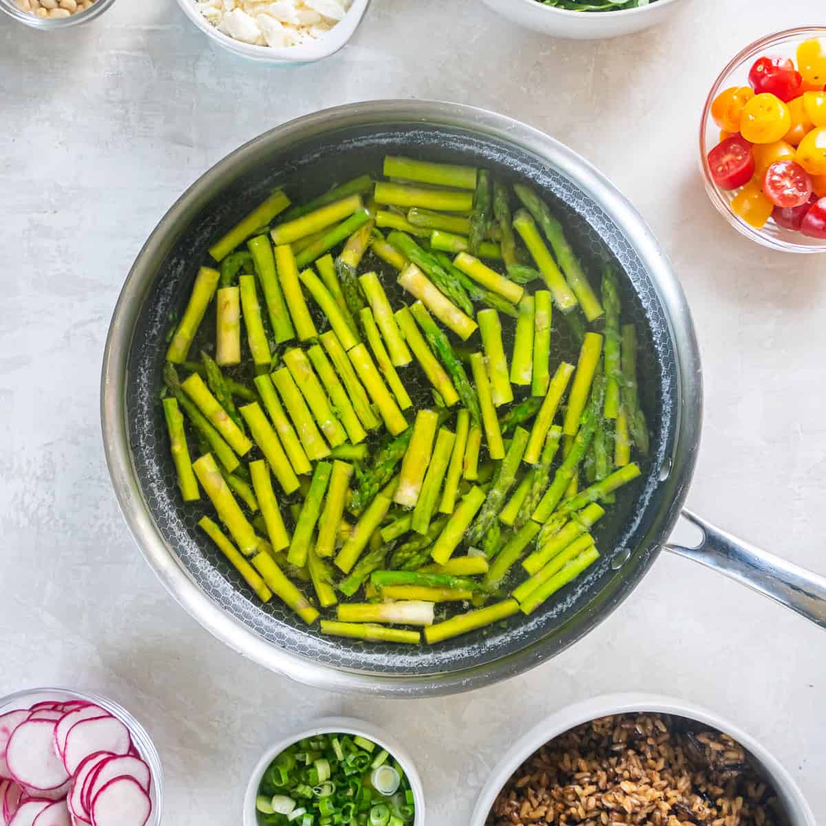 Blanching asparagus pieces in a skillet of simmering water.