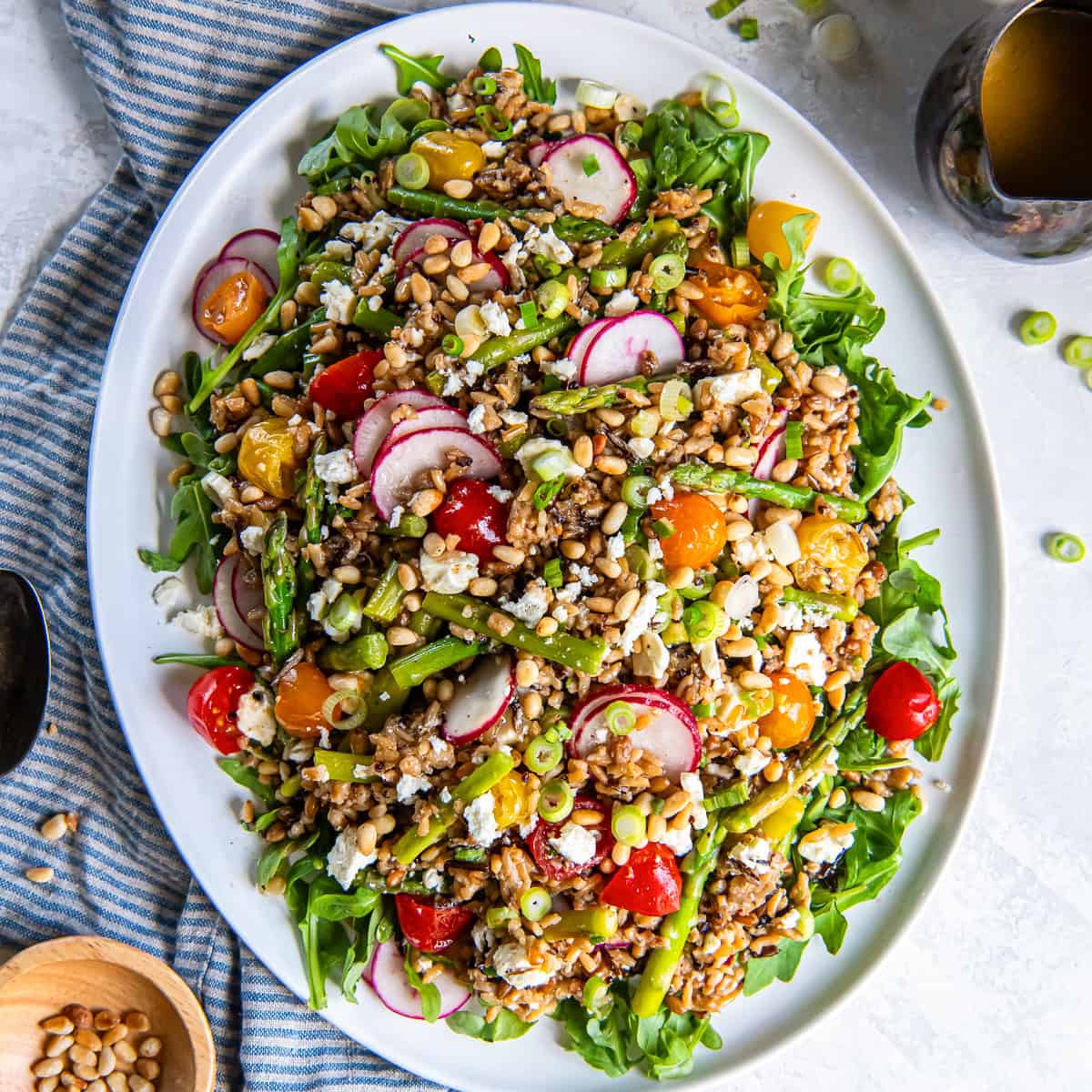 Spring grain salad with asparagus, radishes, tomatoes, goat cheese, pine nuts, and arugula on a white platter.